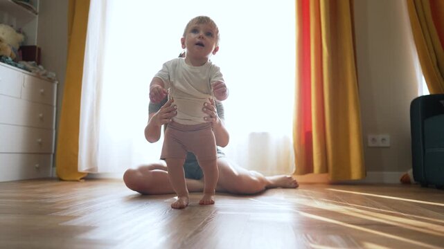 Toddler taking first steps. Mother supports child as toddler learns to step. family moment as toddler confidently makes first steps. Baby milestone as toddler steps forward with mother help indoors.