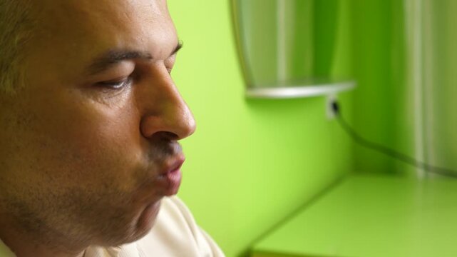 Close up of a man eating a corn puff, slowly taking a bite of a crunchy snack indoors against a green background.