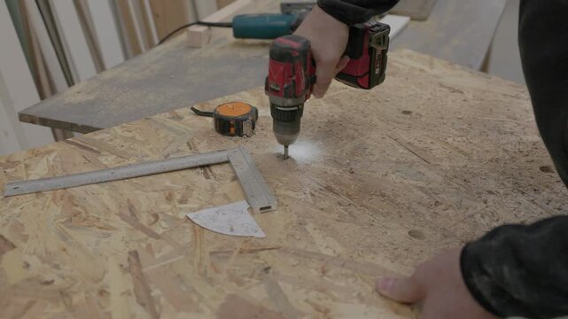 Close-up of worker drilling a hole in an oriented strand board (OSB) panel with a cordless drill during home construction