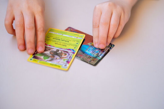 Young enthusiast Child holding Pokemon card, Collecting trading cards with Pokeball logo on white table, close up hands playing, sorting trading card game, Battle with friends, childhood Fan Culture