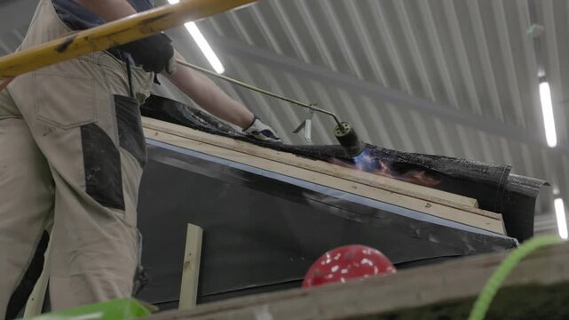 Close-up of flame torch welding modified bitumen roofing membrane on wooden decking during waterproofing installation