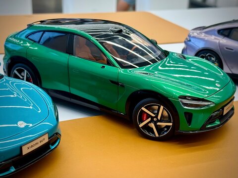 Scale die-cast model of a Xiaomi car, likely the Xiaomi SU7, displayed on a table. The model features a sleek, aerodynamic design with a vibrant green paint job and detailed elements like headlights
