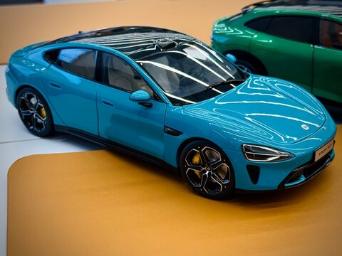 Scale die-cast model of a sleek blue car displayed on a tan surface. The model features detailed design elements like black-tinted windows, aerodynamic contours, and realistic rims 