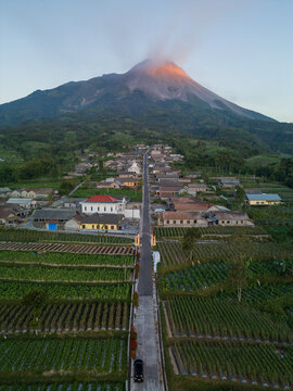 Aerial view of the village of Kecamatan Selo with Rumah Kopi Stabelan, surrounded by lush green fields and Mount Merapi at sunrise, Kecamatan Selo, Jawa Tengah, Indonesia.