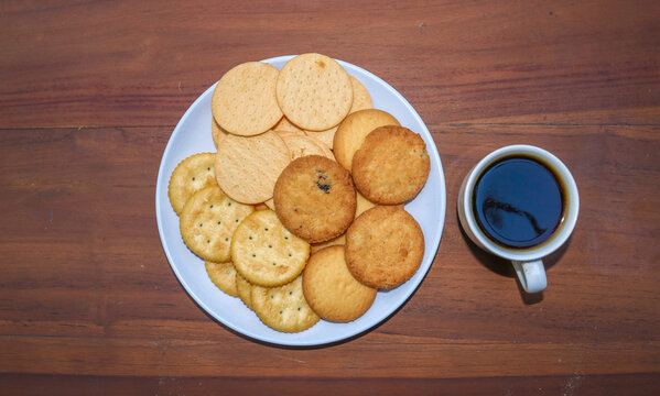 Assorted cookies and biscuits on a plate with black coffee on a wooden table. A collection of sweet baked snacks including chocolate cookies, butter biscuits, crackers
