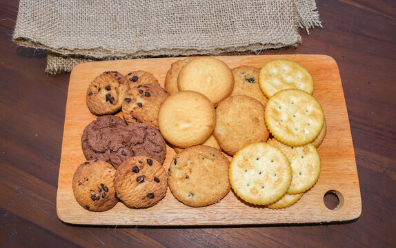 Assorted cookies and biscuits on a wooden board on a wooden table. A collection of sweet baked snacks including chocolate cookies, butter biscuits, crackers, and sandwich cookies on a wooden board.