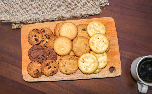 Assorted cookies and biscuits on a wooden board on a wooden table. A collection of sweet baked snacks including chocolate cookies, butter biscuits, crackers, and sandwich cookies on a wooden board.