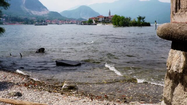 Gentle waves lapping on a pebble shore with the stunning view of isola dei pescatori and the mountains on lake maggiore in stresa