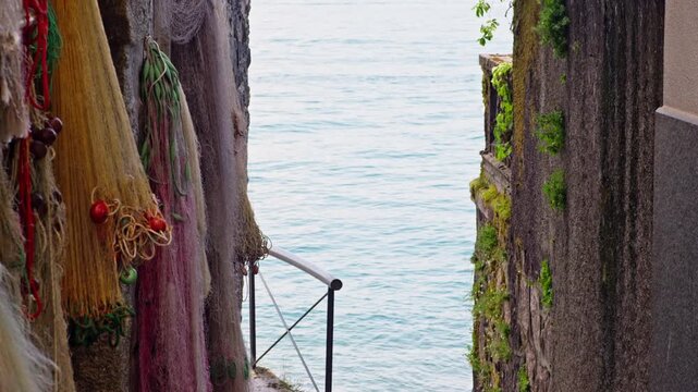 Picturesque alleyway on isola dei pescatori with colorful fishing nets drying on a stone wall. Gentle waves of lake maggiore are visible