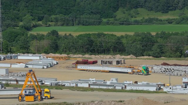 Heavy Transport Truck Hauling Massive Concrete Beams Out Of The Storage Yard, Ascending Drone Flight With Tilt Down