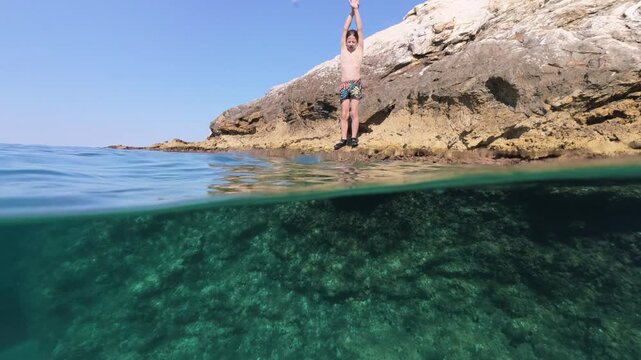 Boy jumping into sea water split shot over under half underwater view
