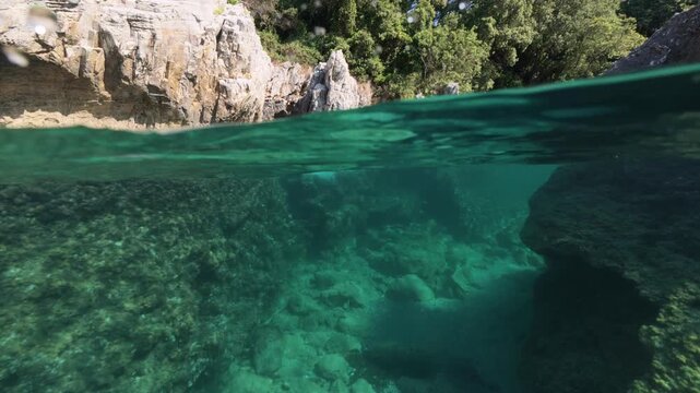 Split shot of rocky coast over under half underwater view of clear sea