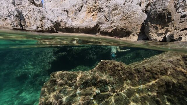 Boy exploring sea cave split shot over under half underwater view