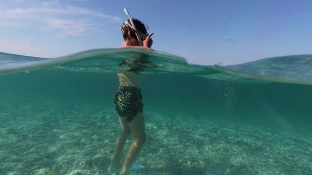 Boy snorkeling in sea split shot over under half underwater