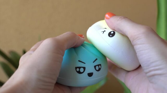 Close-up video of hands squeezing two colorful kawaii squishy stress toys with funny facial expressions. Concept of relaxation, emotional wellness, mindfulness, and anti-stress lifestyle