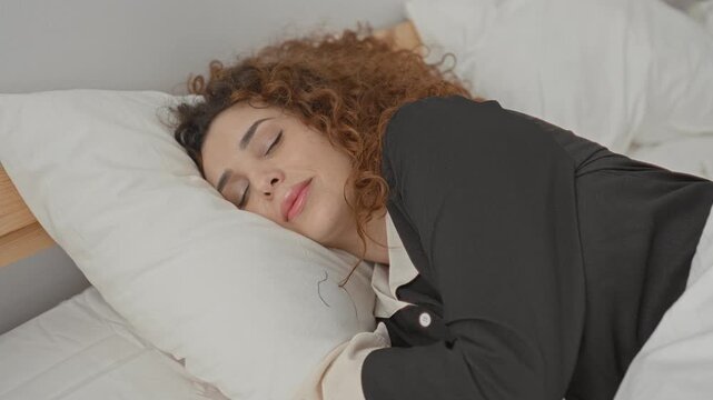 Young hispanic woman sleeping with head on pillow in a studio bed, curly hair visible and relaxed posture; peaceful rest.
