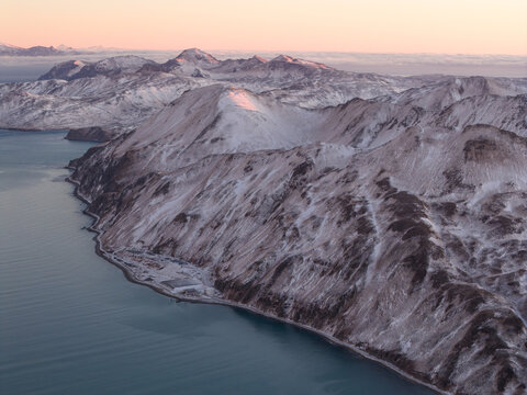 Aerial view of snow-covered mountains along the coastline of Unalaska, Alaska, United States.