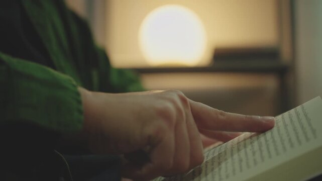 Close-up of Hand Pointing and Tracing Finger Along Text Line While Reading a Book at living room.