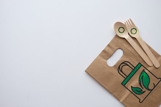 Eco friendly zero waste packaging concept. Top view of brown paper bag and wooden cutlery with recycle icons on white background. Sustainable plastic free food delivery copy space.