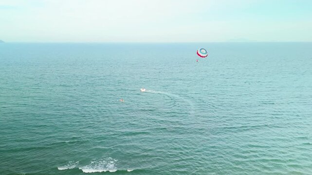 Danang beach in vietnam presenting a lively aerial perspective of vacationers experiencing summer water activities with a parasailer flying high above the calm. Blue sea. A speedboat creating wake