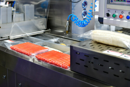 Automated vacuum packaging machine sealing fresh sausages on conveyor line in food processing factory plant