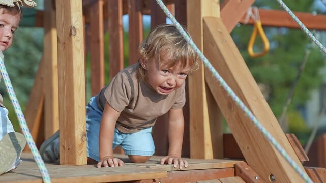 Crying baby on playground upset. Emotional baby expressing frustration outdoors. Upset child on wooden playground. Crying baby feeling upset in summer. Playground tears, upset baby mood. playground.