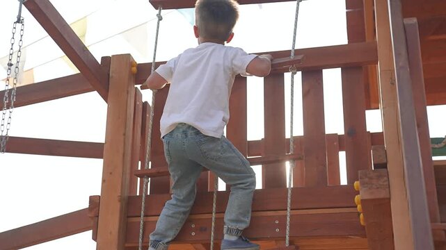 Boy climbing rope in park playground. Active boy play outdoors, enjoying sunny day. Boy pulling rope developing strength and coordination. Fun play for boy in park. Happy childhood, outdoor adventure.