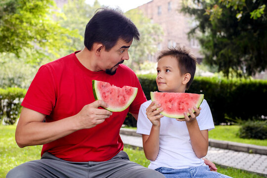 Father and son sharing a joyful summer moment with fresh watermelon in a sunny park. Healthy family lifestyle, outdoor recreation, childhood memories, and strong family bonds