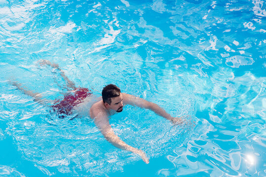 Athletic man swimming in a clear blue pool on a sunny day. Healthy lifestyle, fitness training, recreation, and summer vacation concept with copy space