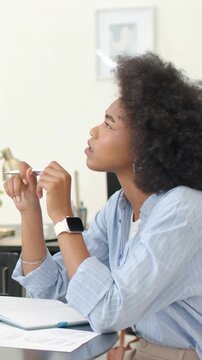 Vertical video: Lifting pen, African woman in striped shirt thinking at study table with notebook