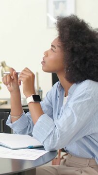 Vertical video: Listening to offscreen voice, woman in blue shirt holding pen and focusing at desk