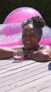 Vertical video: Smiling elder on pool deck waving to offframe hand entering dark tank float drink