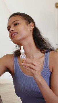 Vertical video: Reacting to cue woman in ribbed top holding dropper at home demonstrating product