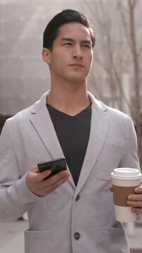 Vertical video: Commuting man in gray blazer in plaza checking phone and scanning area holding cup
