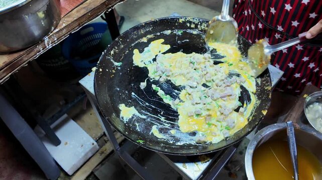 Thai street food vendor adds diced taro cubes onto an egg pancake while cooking on a hot flat griddle at a local night market in Thailand. Authentic Asian street food preparation captured in 4K.