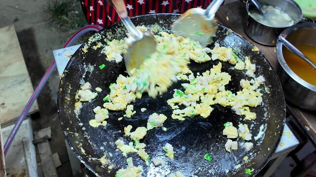Close-up of a Thai street food vendor scrambling eggs with diced taro and chopped green onions on a large flat griddle at a local night market. Authentic traditional street food preparation in Thailan