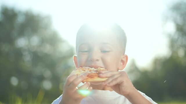 Happy child enjoying pizza at picnic in park. Boy smiling while eating pizza outdoors. Fun picnic with child in sunny park. Child savoring pizza slice during outdoor meal. Joyful park day with pizza.