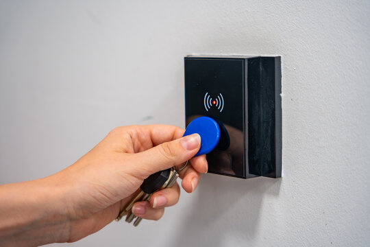 Person using contactless key fob on indoor access control reader. Secure building access protects restricted areas and residential facilities