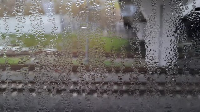 Close-up of wet window glass covered with condensation droplets. Blurry railway tracks and misty outdoor platform through foggy train window. Train ride, railway infrastructure behind glass