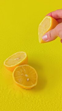 Female hand squeezing fresh juice from a lemon half against a solid yellow background. Clean minimalist food commercial and wellness concept.