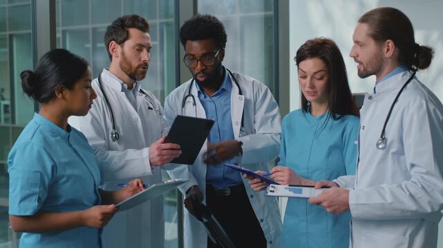 Group of five multiracial medical doctors emotional talking with digital tablet device and lung x-ray medicine results. African American leader doctor consulting multiethnic colleagues interns talk