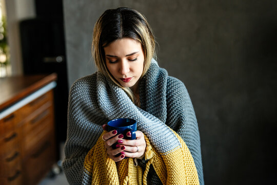Sick woman shivering from cold, drinking hot tea in unheated home apartment without heating due debt