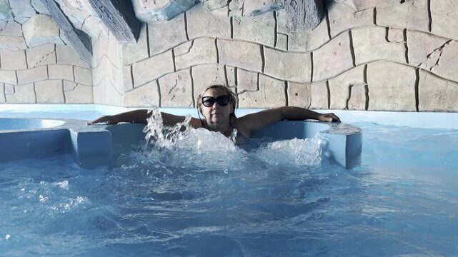 Person relaxing in indoor pool with sunglasses
