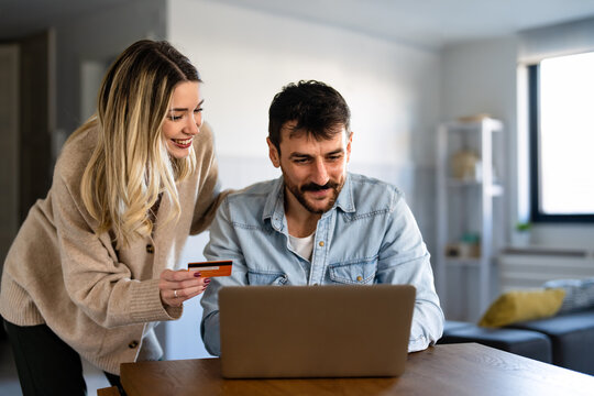 Smiling happy couple managing their personal finance at home with laptop and credit card