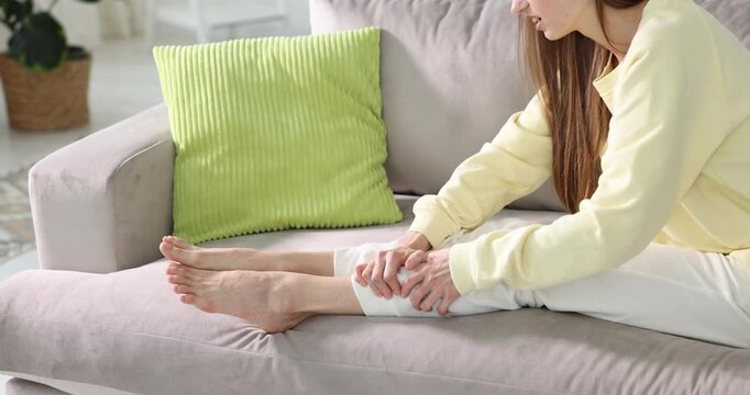 Woman suffering from leg pain on sofa at home, closeup