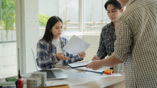 A team of young Asian architects and engineers is discussing project plans and layouts, using laptops to review architectural designs and construction site development plans.