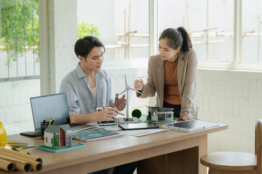 Business partners are discussing ESG strategies and renewable energy projects, using laptops and a wind turbine model to plan green energy investments.
