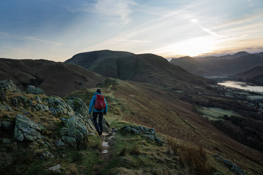 A female hiker walking over Rannerdale Knotts, Low Bank at dawn on a winters day in the Lake District, Cumbria, England, UK.