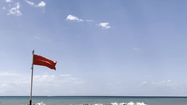 Red warning flag waving on a beach during strong wind, signaling dangerous sea conditions and high surf hazards