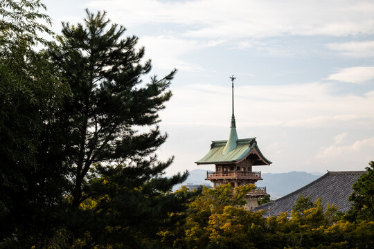 Gion-kaku (Copper Pavilion), a 36-meter tall tower inside the Daiun-in Temple in Kyoto, framed by trees against a cloudy sky